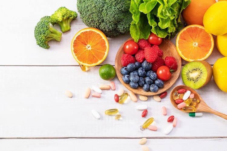 Surtido de frutas naturales y cáspsulas de suplementos nutricionales en cuchara de madera