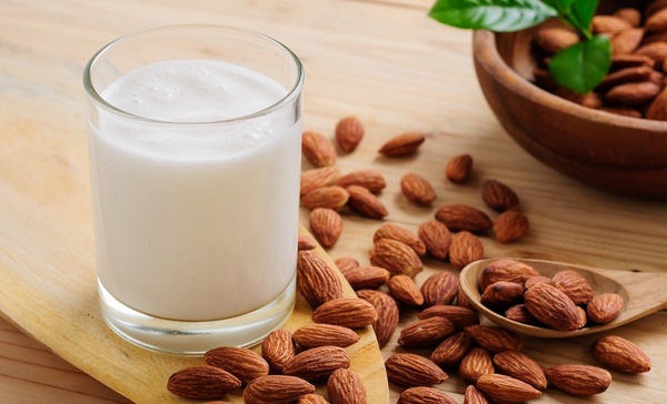 Vaso con leche de almendras, almendras larguetas crudas con piel y cuenco con almendras depositados sobre una mesa