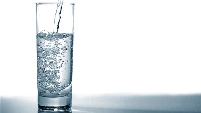 Chorro de agua vertido sobre vaso de agua de cristal