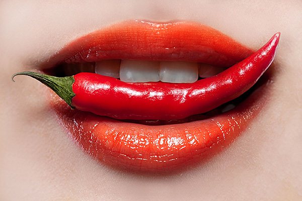 Labios de mujer sujetando una guindilla roja