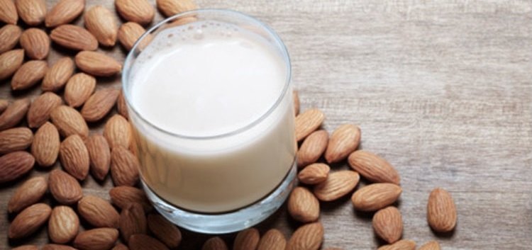 Imagen de un vaso de leche de almendras y varias almendras en sus inmediaciones