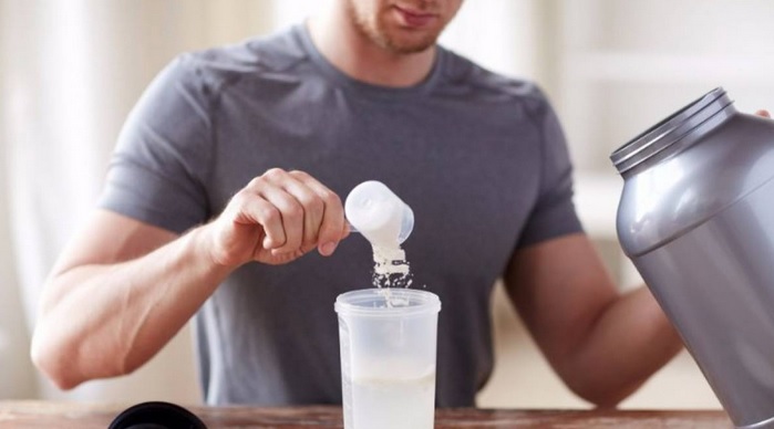 Hombre añadiendo un cacillo de proteína en polvo en un shaker para proteínas