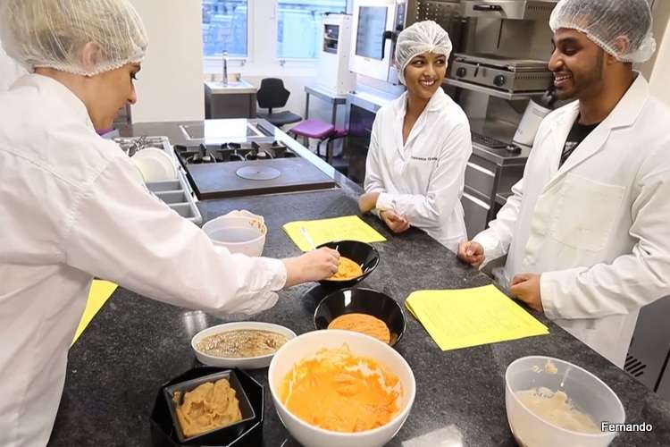 Tres dietistas-nutricionistas provistos de bata y malla para el pelo manipulando alimentos